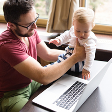 Dad playing with a baby next to a laptop.