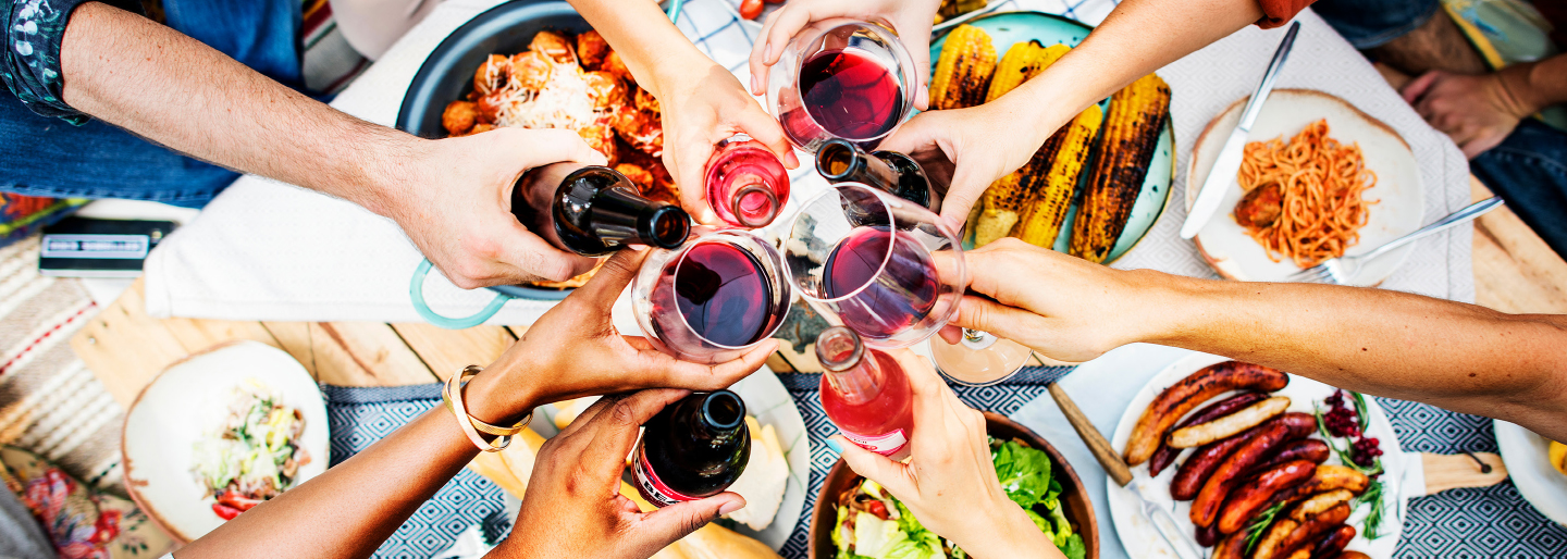 hands with wine glasses and bottles in middle of table on top of food and plates below