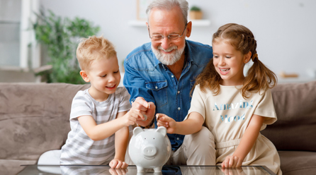 Man sitting with two children putting coins in a piggy bank
